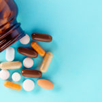 Heap of colorful medical pills and tablets spilling out of a drug bottle on blue background. Top down view with copy space.