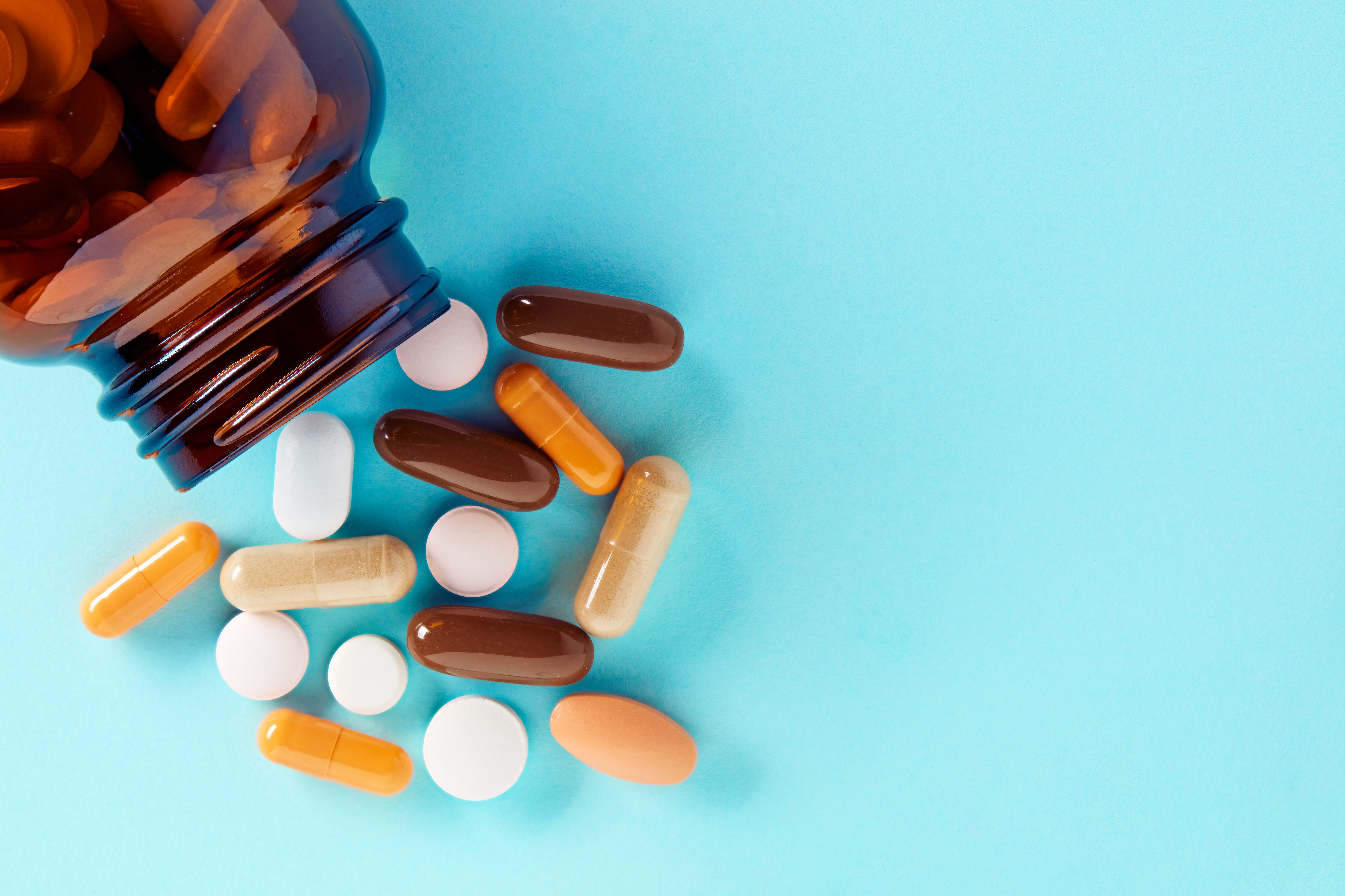 Heap of colorful medical pills and tablets spilling out of a drug bottle on blue background. Top down view with copy space.